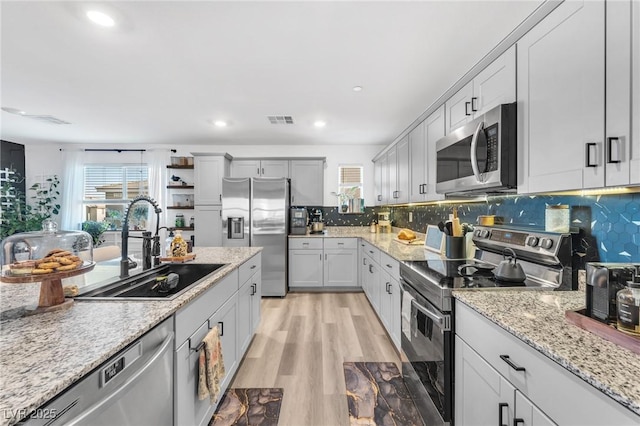 kitchen featuring decorative backsplash, sink, light wood-type flooring, light stone countertops, and stainless steel appliances