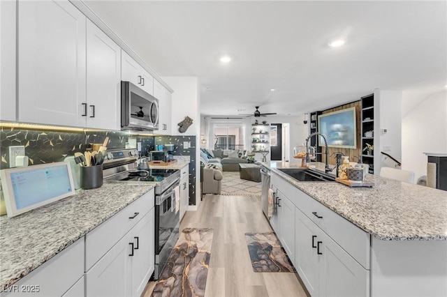 kitchen with ceiling fan, white cabinetry, stainless steel appliances, and a kitchen island with sink