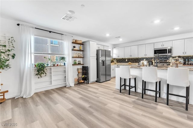 kitchen featuring light stone countertops, white cabinetry, stainless steel appliances, a kitchen breakfast bar, and light wood-type flooring