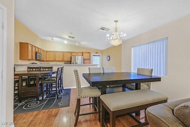 dining room featuring wood-type flooring, lofted ceiling, and a notable chandelier