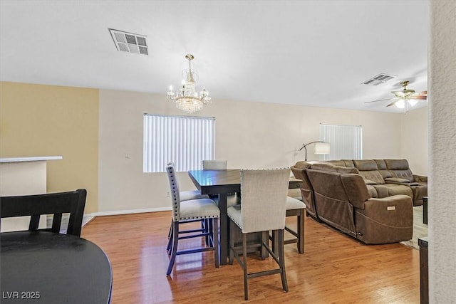 dining space with light wood-type flooring and ceiling fan with notable chandelier