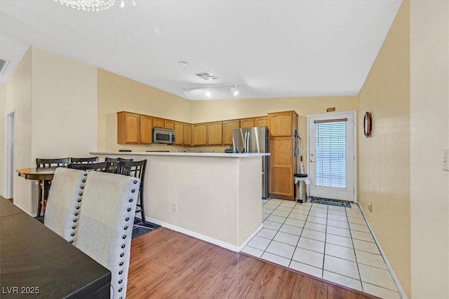 kitchen with lofted ceiling, kitchen peninsula, stainless steel appliances, and light hardwood / wood-style floors