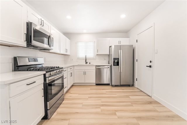 kitchen featuring white cabinets, stainless steel appliances, sink, light wood-type flooring, and light stone counters