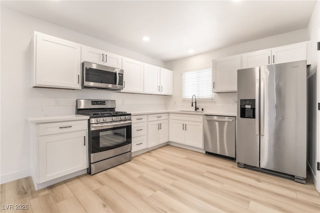 kitchen with stainless steel appliances, light hardwood / wood-style flooring, white cabinetry, and sink