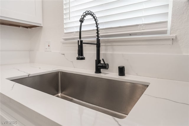 interior details featuring light stone countertops, white cabinets, and sink