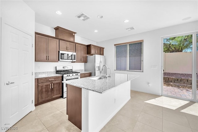 5640 Akula Bay St, North Las Vegas, NV 89081 - kitchen featuring appliances with stainless steel finishes, a sink, light tile patterned floors, a center island with sink, and light stone counters