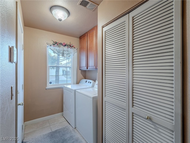 clothes washing area featuring washer and dryer, cabinets, a textured ceiling, and light tile patterned flooring