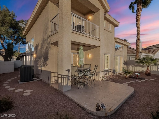 back house at dusk featuring a patio area, a balcony, and central air condition unit