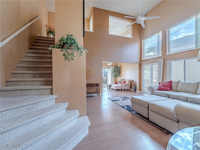 living room with light wood-type flooring, ceiling fan, and a towering ceiling