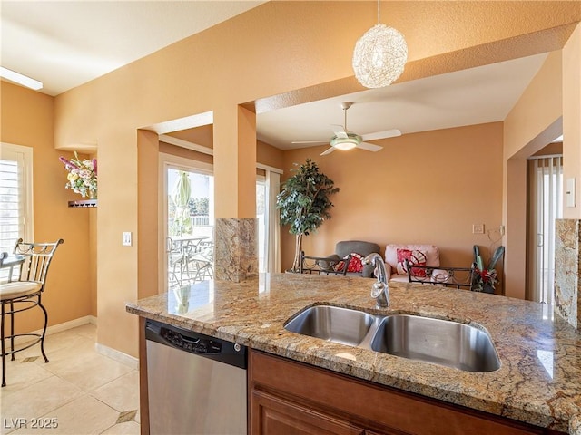 kitchen featuring light stone countertops, decorative light fixtures, sink, light tile patterned floors, and stainless steel dishwasher