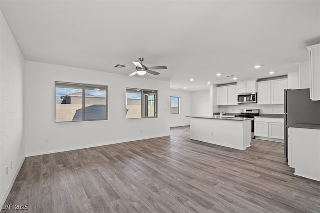 kitchen with appliances with stainless steel finishes, white cabinetry, ceiling fan, light hardwood / wood-style flooring, and a center island with sink