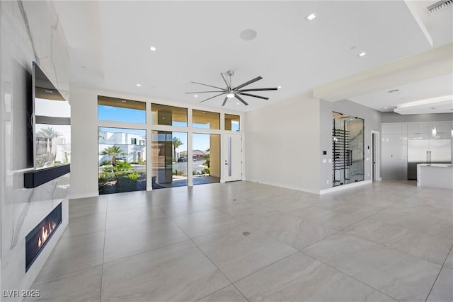 unfurnished living room with ceiling fan, a large fireplace, and floor to ceiling windows