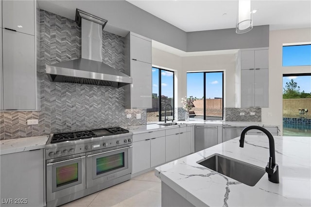 kitchen featuring stainless steel appliances, wall chimney exhaust hood, light stone counters, and sink