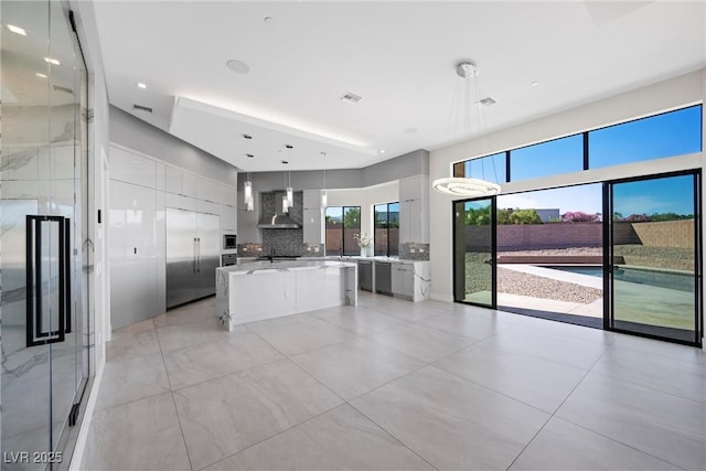 kitchen featuring a center island, pendant lighting, built in appliances, white cabinets, and wall chimney exhaust hood