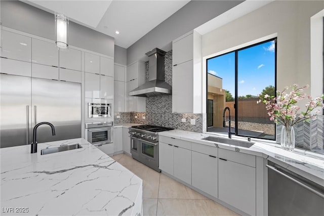 kitchen with hanging light fixtures, sink, wall chimney range hood, and high end appliances