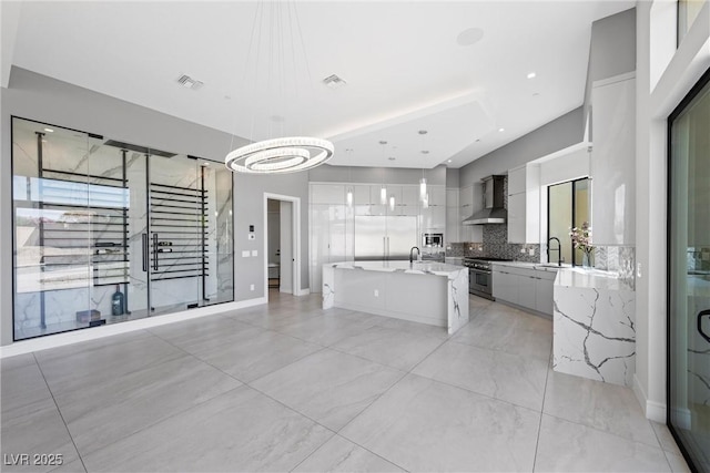 kitchen featuring a kitchen island, sink, built in appliances, hanging light fixtures, and wall chimney exhaust hood