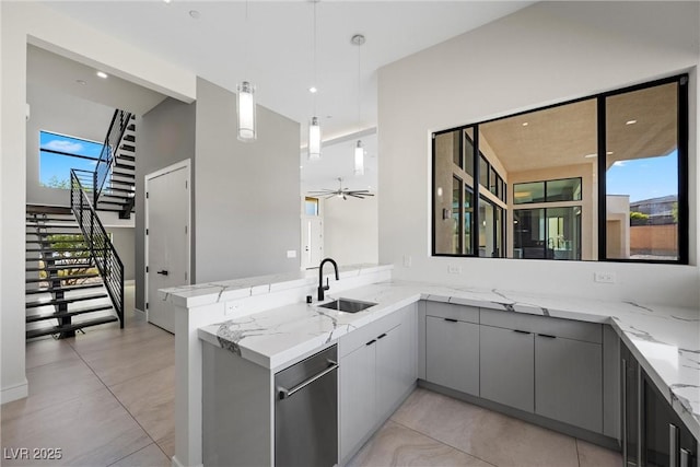 kitchen with kitchen peninsula, sink, hanging light fixtures, light stone countertops, and gray cabinetry