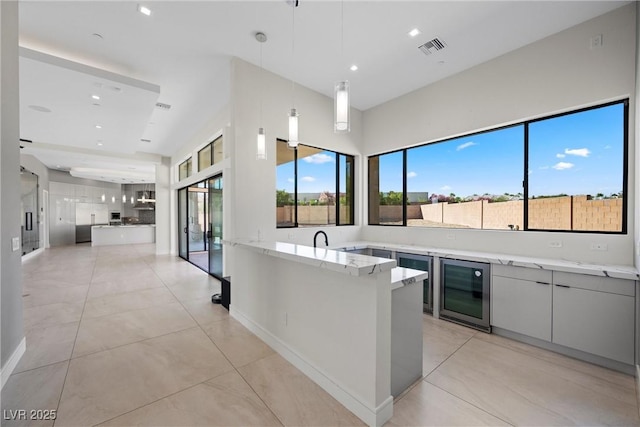 kitchen featuring kitchen peninsula, light tile patterned flooring, wine cooler, light stone countertops, and pendant lighting