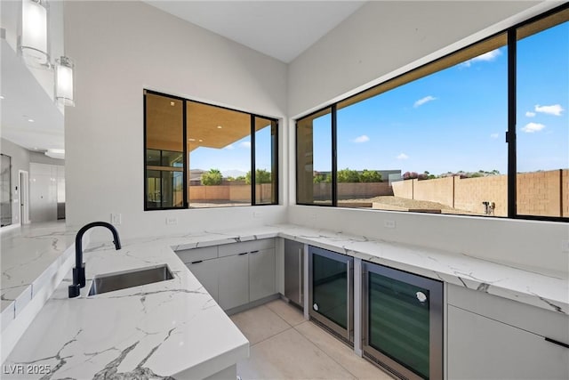 kitchen featuring wine cooler, kitchen peninsula, sink, and light stone counters