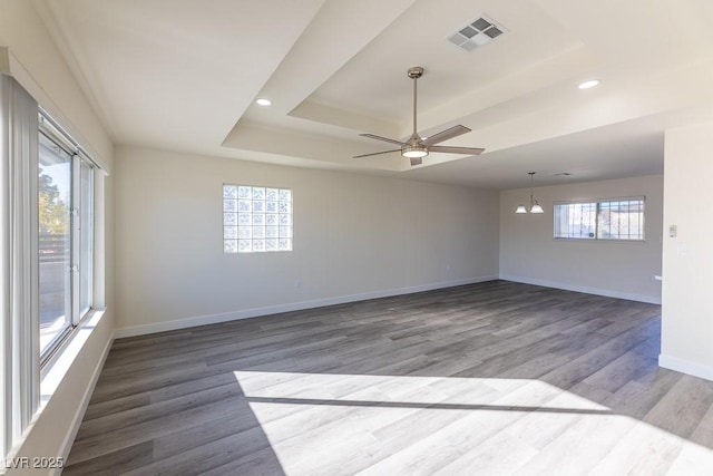 unfurnished room with ceiling fan with notable chandelier, hardwood / wood-style floors, and a raised ceiling