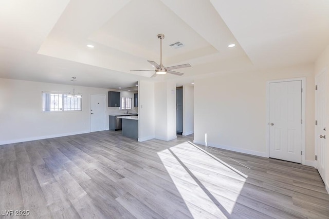 unfurnished living room featuring light hardwood / wood-style floors, a raised ceiling, and ceiling fan