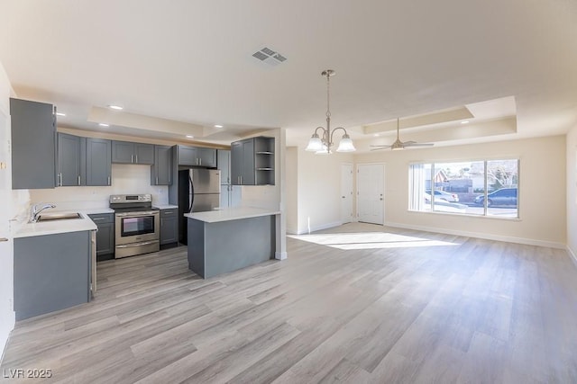 kitchen with decorative light fixtures, gray cabinets, a raised ceiling, appliances with stainless steel finishes, and ceiling fan with notable chandelier