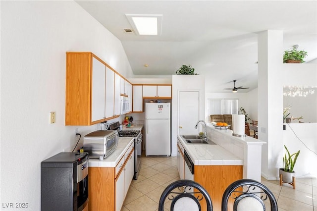 kitchen with ceiling fan, tile counters, white appliances, vaulted ceiling, and sink