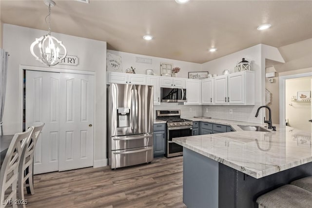 kitchen featuring kitchen peninsula, sink, white cabinetry, hanging light fixtures, and stainless steel appliances