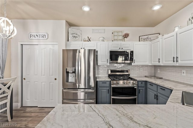 kitchen featuring light stone countertops, white cabinets, decorative light fixtures, stainless steel appliances, and gray cabinetry