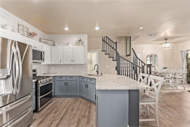 kitchen featuring decorative light fixtures, light hardwood / wood-style floors, sink, stainless steel appliances, and white cabinets