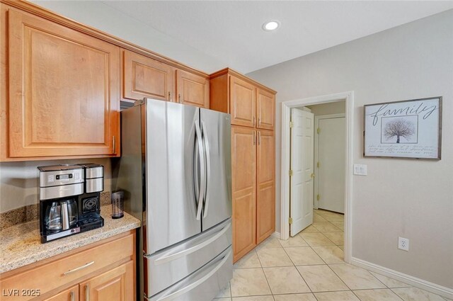 kitchen with light tile patterned floors, light stone countertops, and stainless steel refrigerator