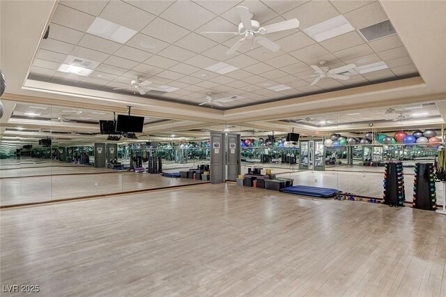 gym featuring ceiling fan, a paneled ceiling, wood-type flooring, and a tray ceiling