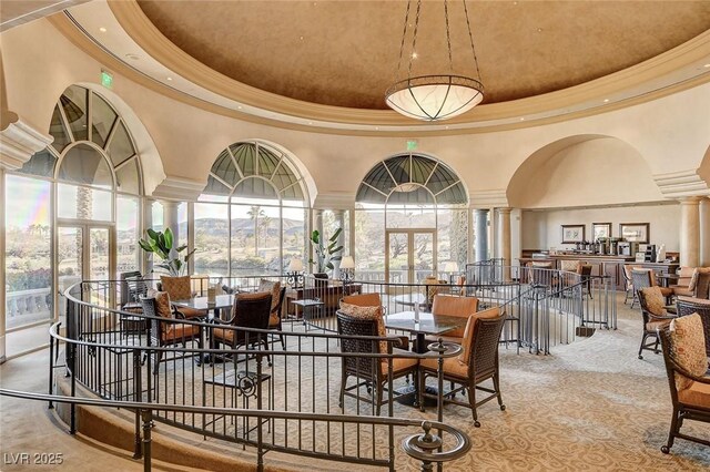 carpeted dining space with decorative columns, a tray ceiling, ornamental molding, and a towering ceiling