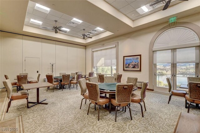 carpeted dining space featuring ceiling fan, a drop ceiling, a high ceiling, and a raised ceiling