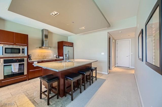 kitchen with appliances with stainless steel finishes, wall chimney range hood, sink, a breakfast bar, and a center island with sink