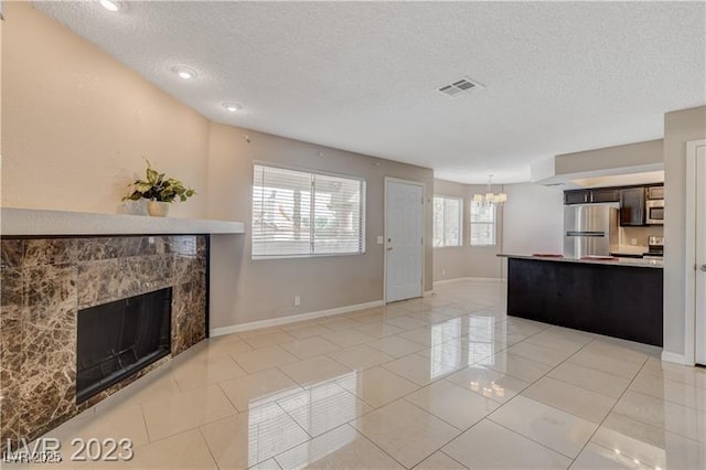 unfurnished living room featuring a textured ceiling, a tile fireplace, and a notable chandelier