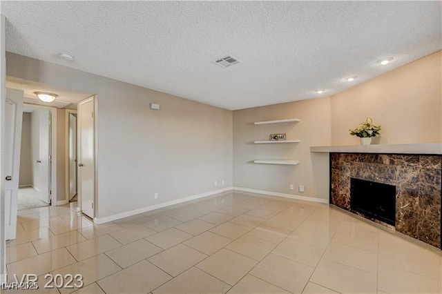 unfurnished living room with a tiled fireplace, light tile patterned flooring, and a textured ceiling