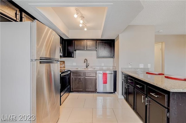 kitchen with appliances with stainless steel finishes, sink, a raised ceiling, light tile patterned flooring, and light stone counters