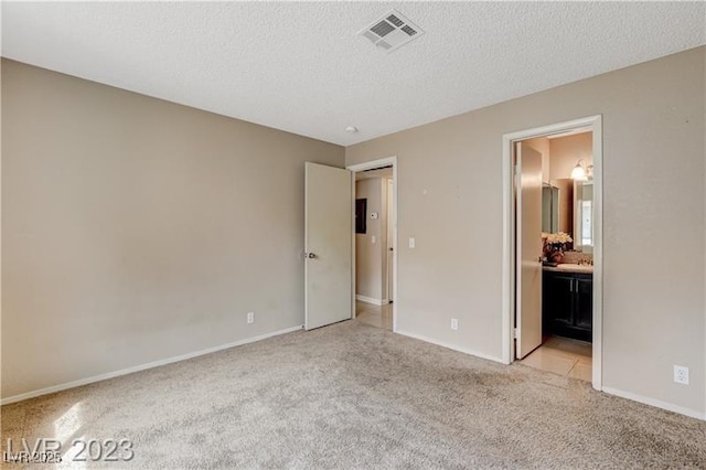 unfurnished bedroom with a textured ceiling, ensuite bathroom, and light colored carpet