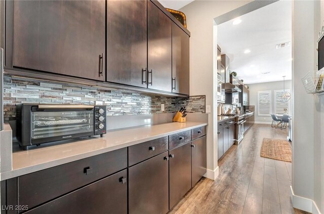 kitchen with backsplash, dark brown cabinetry, hanging light fixtures, and light wood-type flooring