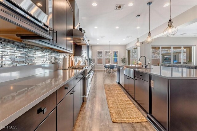 kitchen featuring extractor fan, tasteful backsplash, light wood-type flooring, hanging light fixtures, and sink