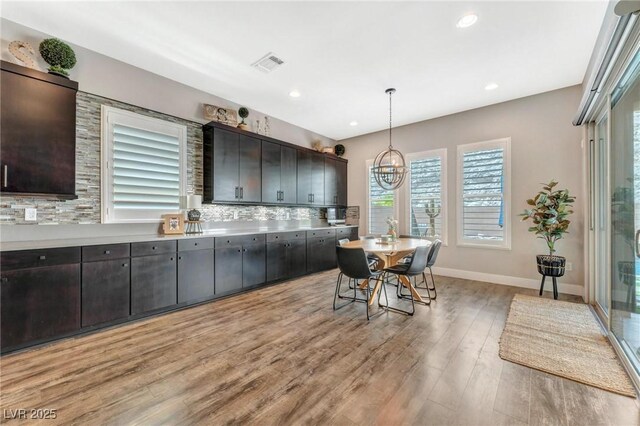 kitchen featuring a notable chandelier, light hardwood / wood-style floors, a breakfast bar, decorative backsplash, and hanging light fixtures