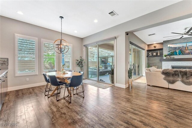 dining space with built in features, dark hardwood / wood-style flooring, ceiling fan with notable chandelier, and a large fireplace