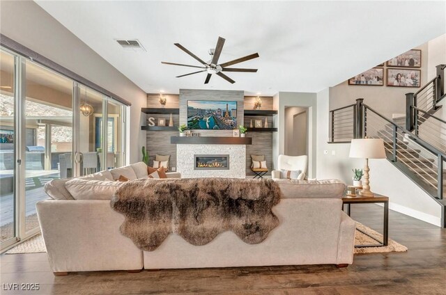 living room with ceiling fan, dark hardwood / wood-style flooring, built in features, and a stone fireplace