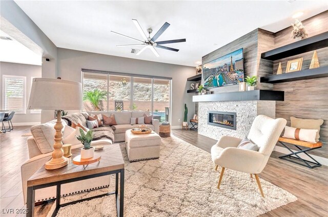 living room featuring ceiling fan, a wealth of natural light, a stone fireplace, and hardwood / wood-style flooring