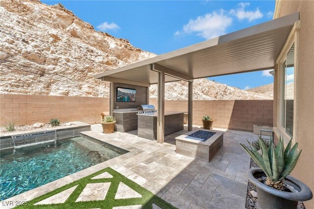 view of patio / terrace with a mountain view, an outdoor fire pit, exterior kitchen, a fenced in pool, and pool water feature