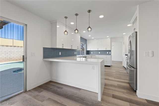 kitchen with decorative light fixtures, white cabinetry, tasteful backsplash, kitchen peninsula, and stainless steel refrigerator