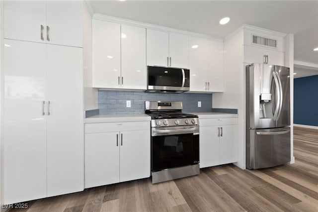 kitchen featuring tasteful backsplash, white cabinets, stainless steel appliances, and hardwood / wood-style flooring