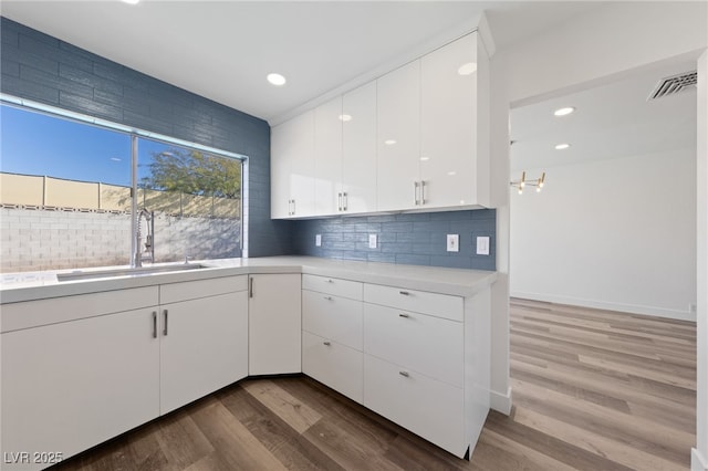 kitchen with decorative backsplash, light hardwood / wood-style floors, white cabinets, and sink