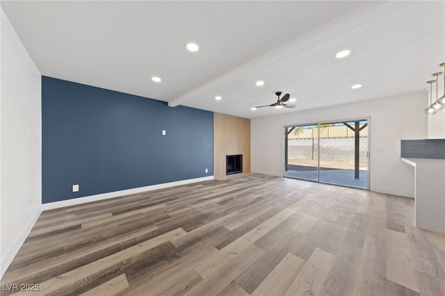 unfurnished living room featuring ceiling fan, a fireplace, hardwood / wood-style flooring, and beamed ceiling